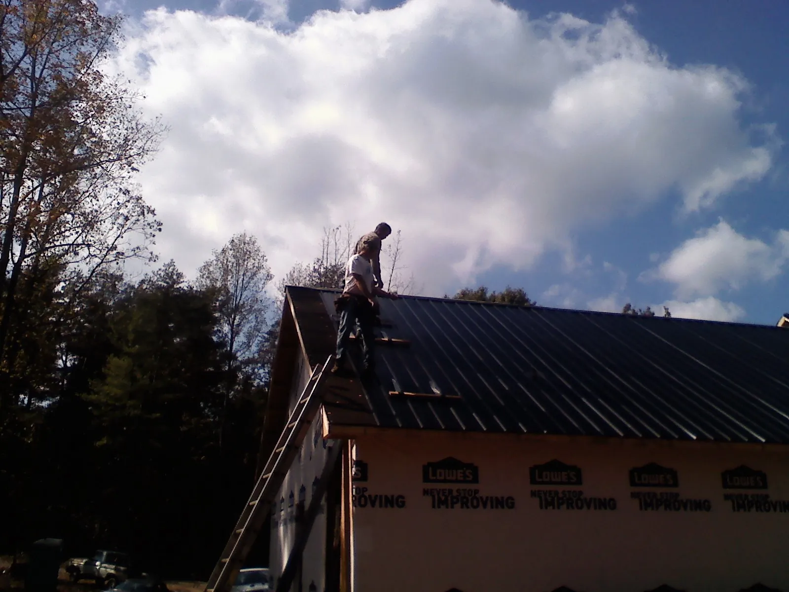Roofer fastening dark metal panels high against a cloudy sky, from a Roof Inspection job in Westfield